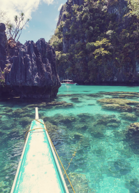 A boat rests on the water near a rugged shore in Palawan, Philippines, showcasing the coastal beauty.